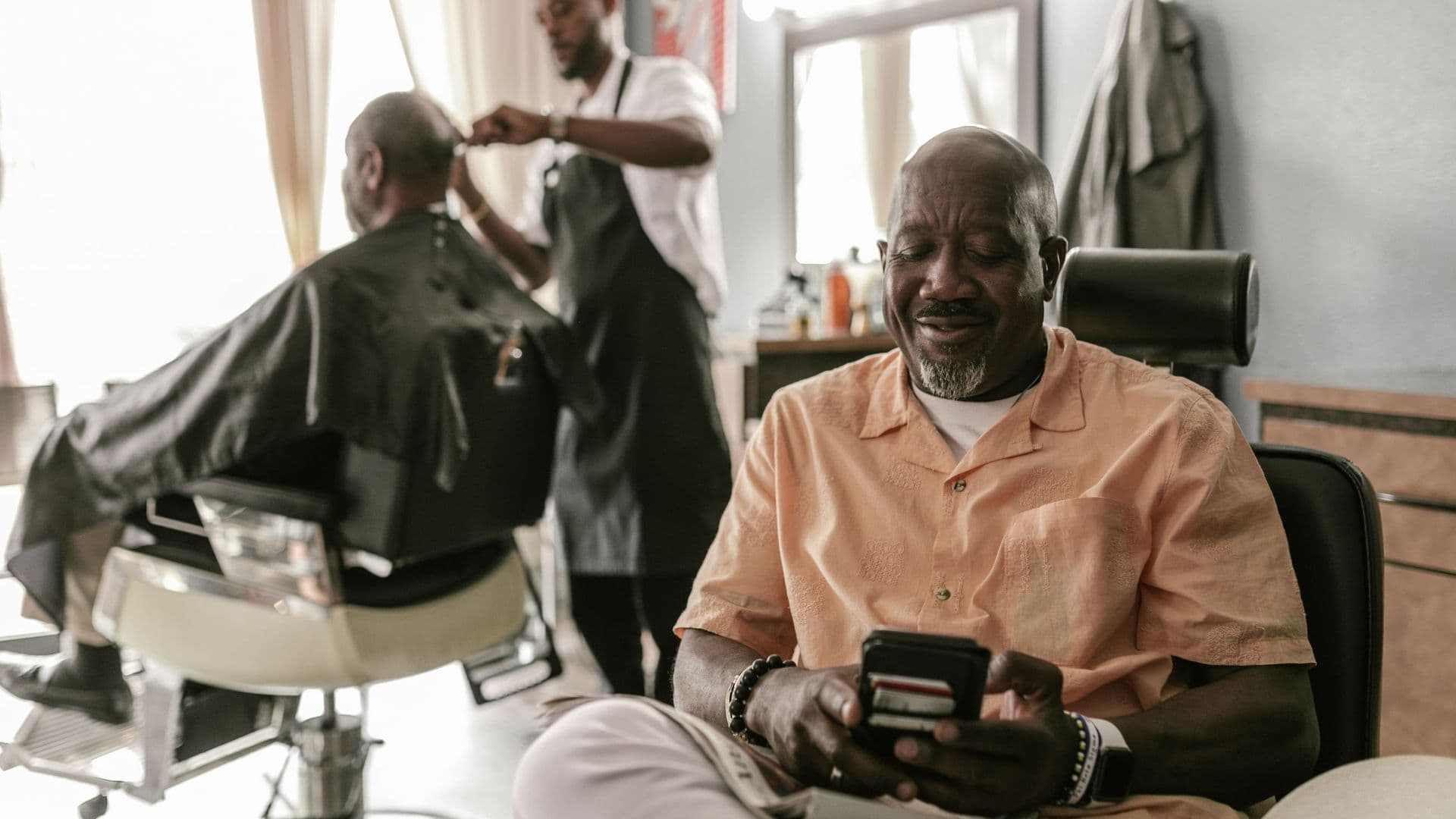 Cliente a usar o telemóvel numa barbearia enquanto outro cliente corta o cabelo