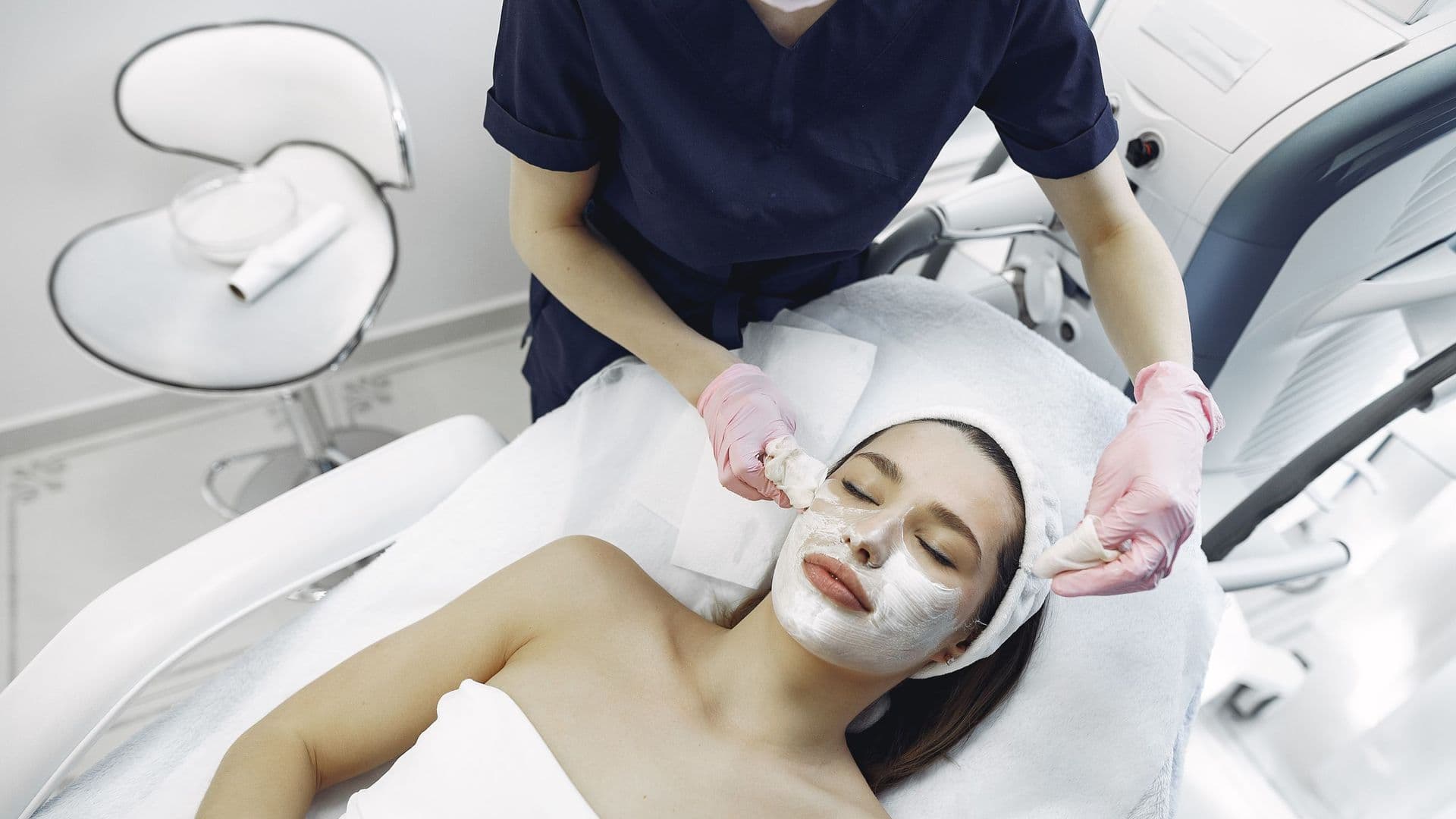 Esteticista de luvas a retirar uma máscara facial a uma cliente deitada numa marquesa