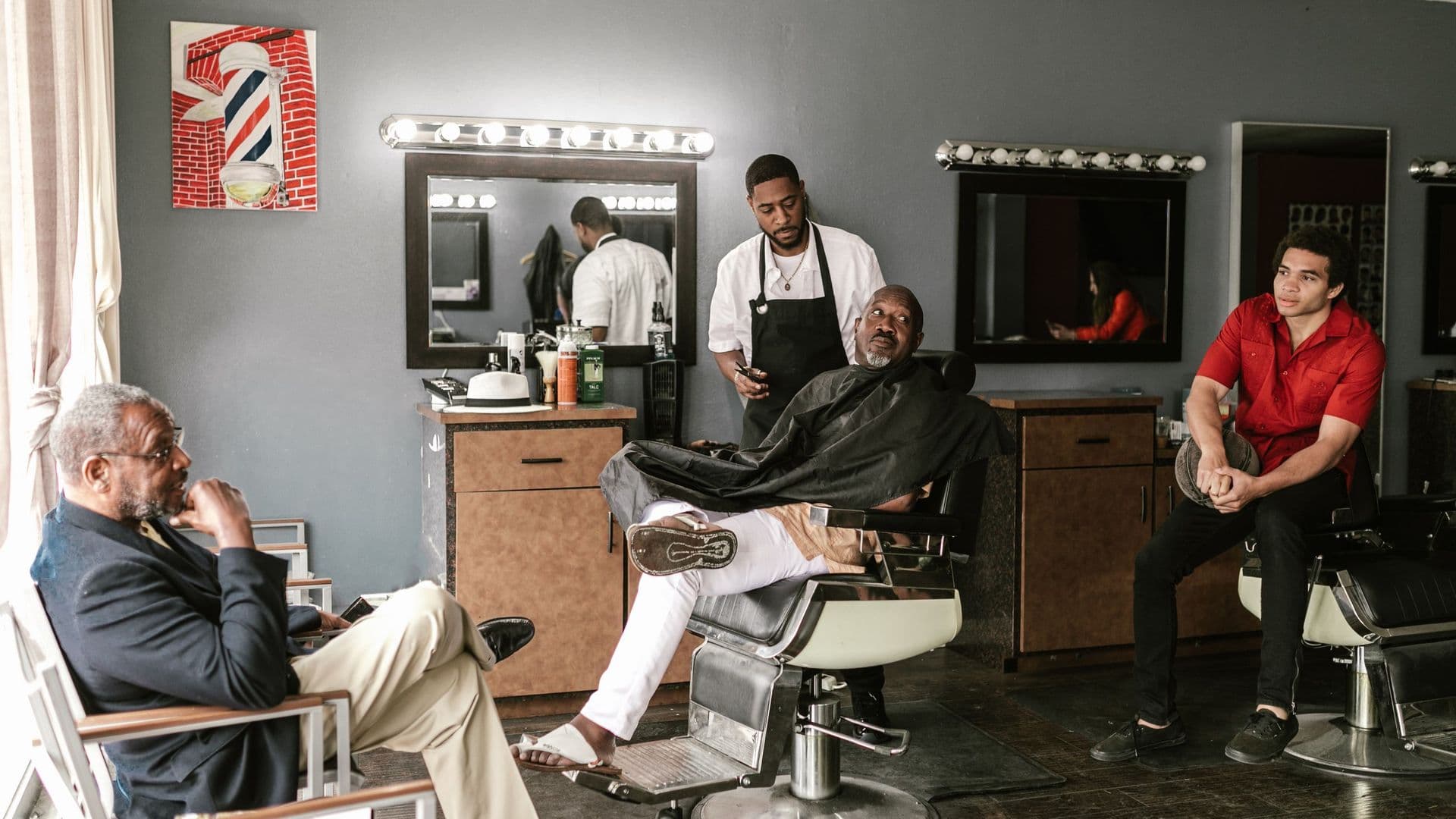 Barbearia com clientes a conversar enquanto um barbeiro corta o cabelo