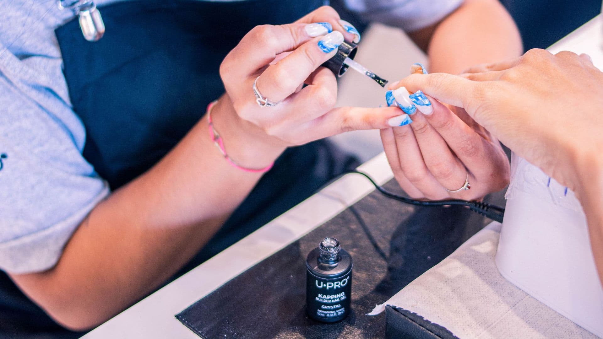 Nail designer a aplicar verniz nas unhas decoradas de azul de uma cliente