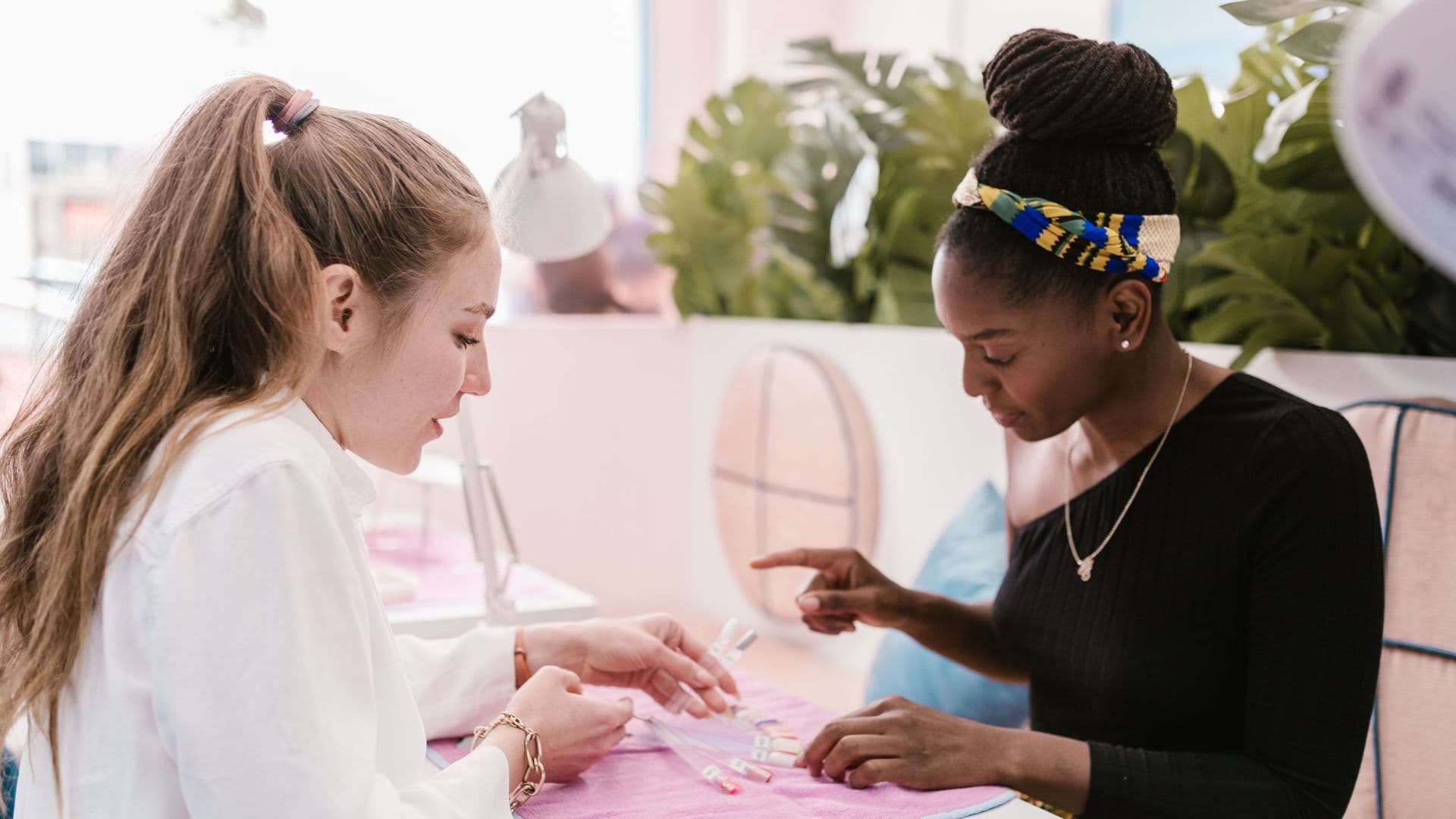 Duas mulheres a escolher cores de verniz numa mesa de manicure