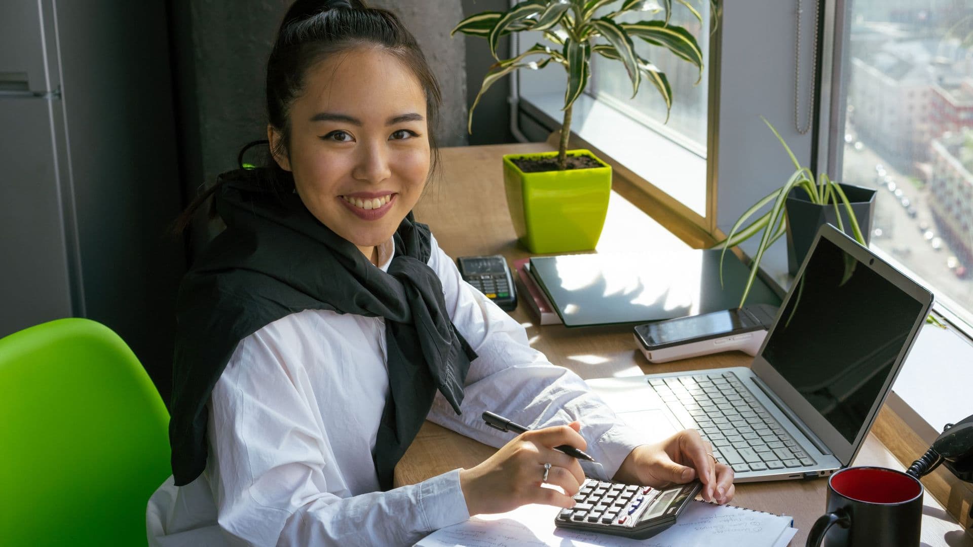 Mulher sorridente a trabalhar com calculadora e portátil numa secretária