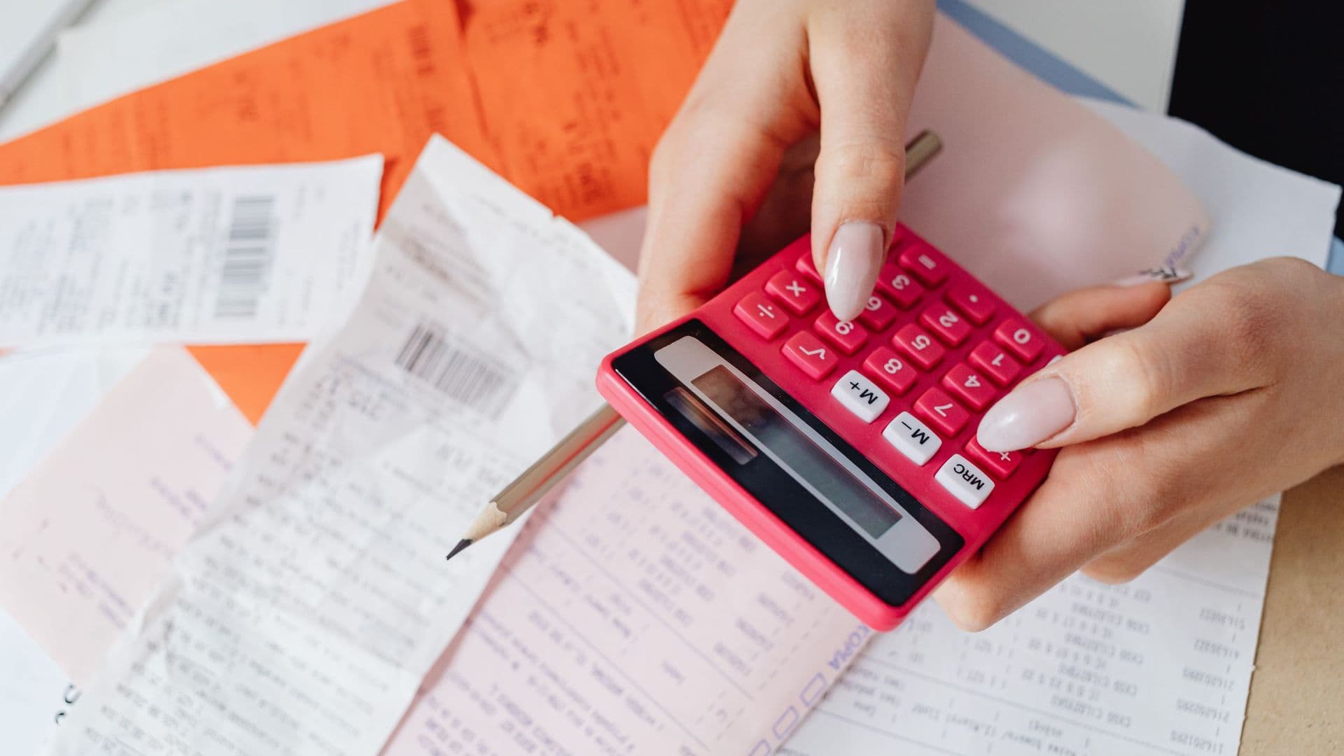 Mãos a usar uma calculadora cor-de-rosa sobre faturas e recibos