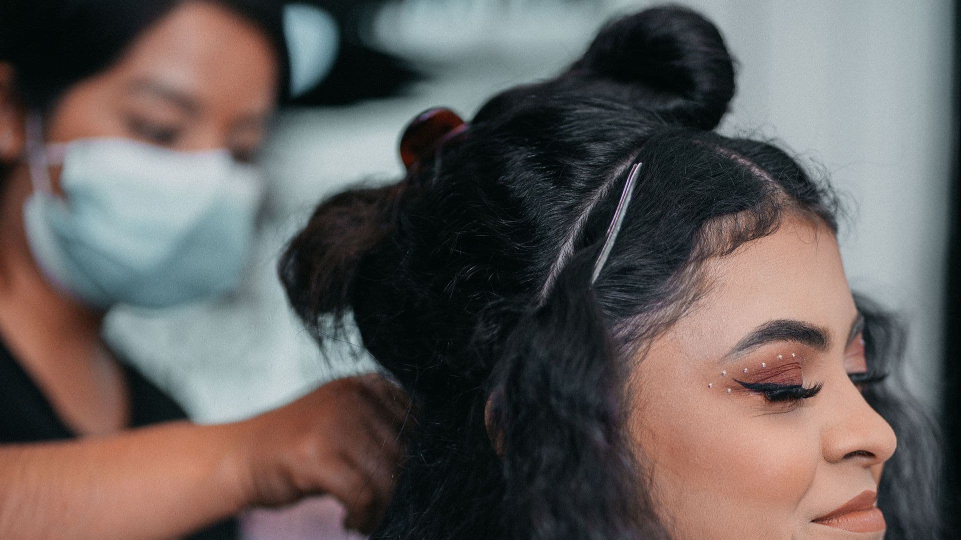 Cabeleireira de máscara fazendo um penteado em uma cliente maquiada