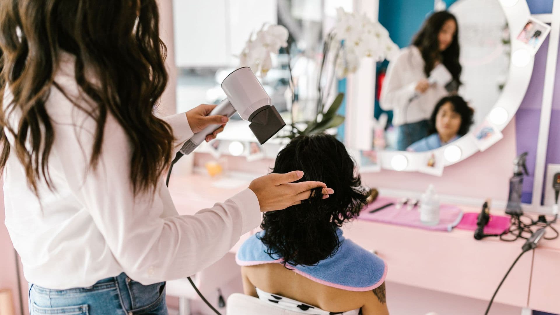 Cabeleireira secando o cabelo de uma cliente em um salão com espelho