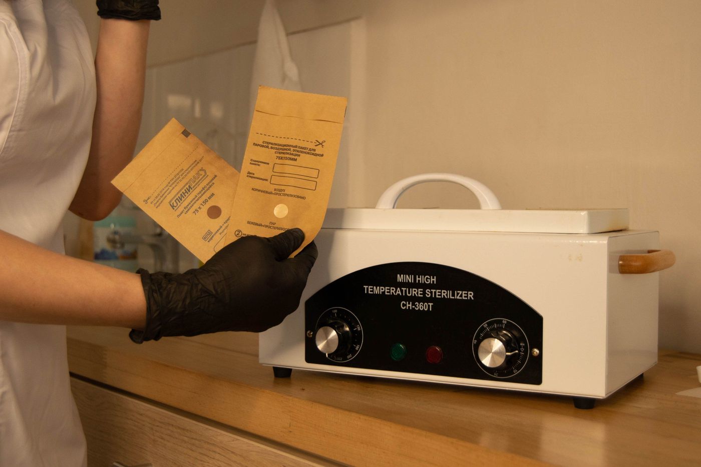 Profissional de luvas colocando embalagens de esterilização ao lado de uma estufa