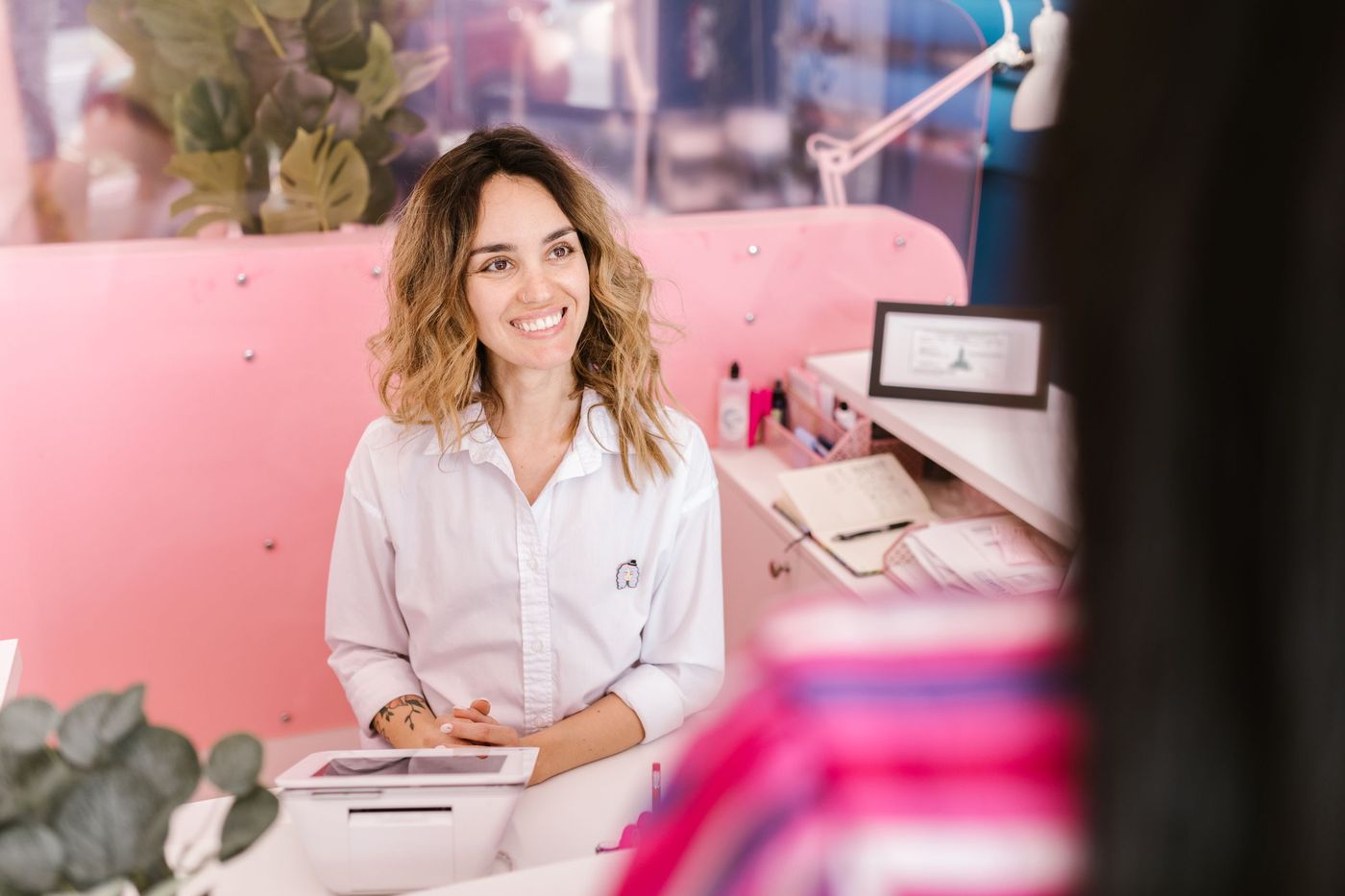 Rececionista sorridente ao balcão de um salão com tablet