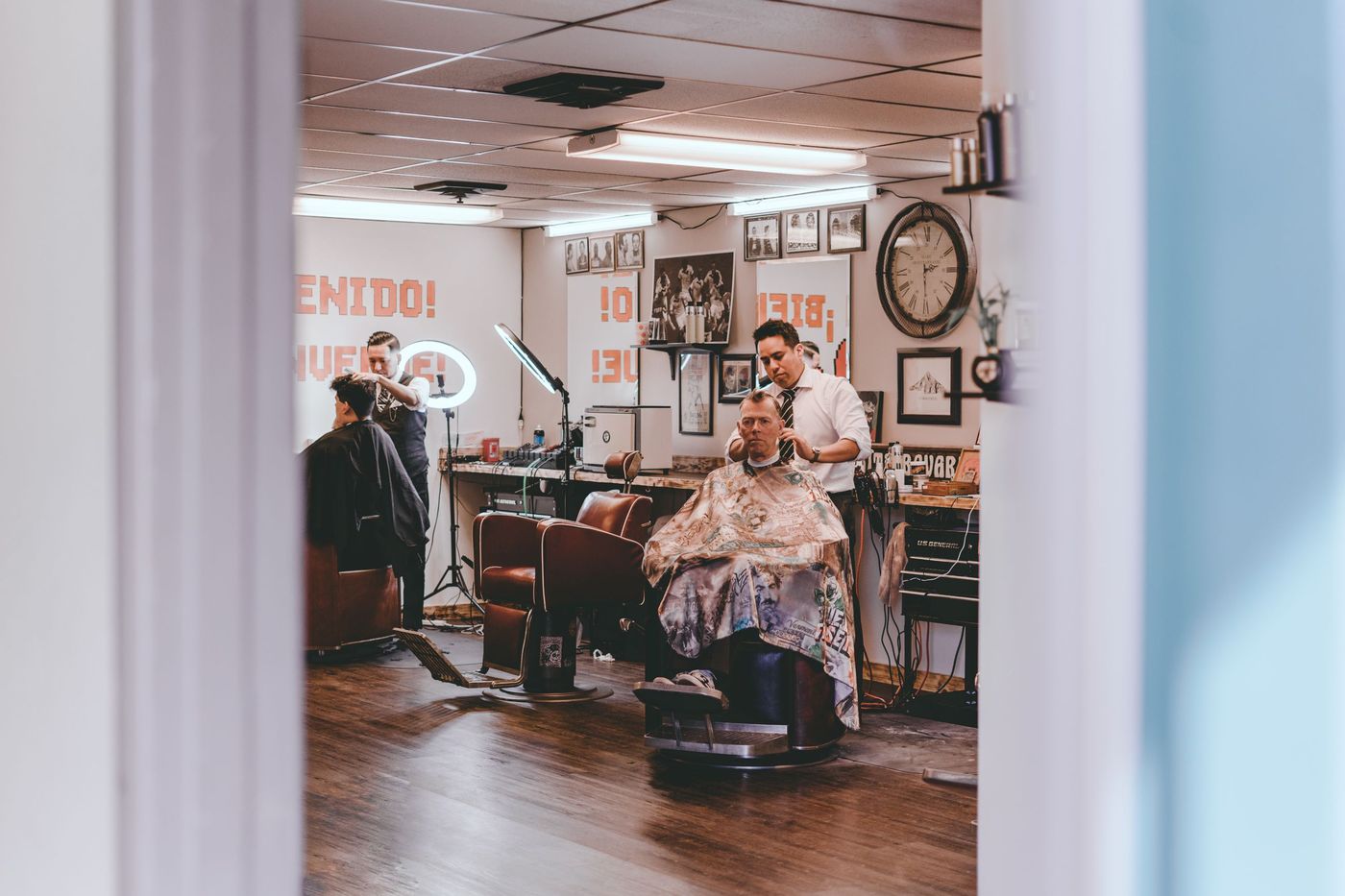 Barbeiros atendendo clientes em uma barbearia com cadeiras de couro e piso de madeira