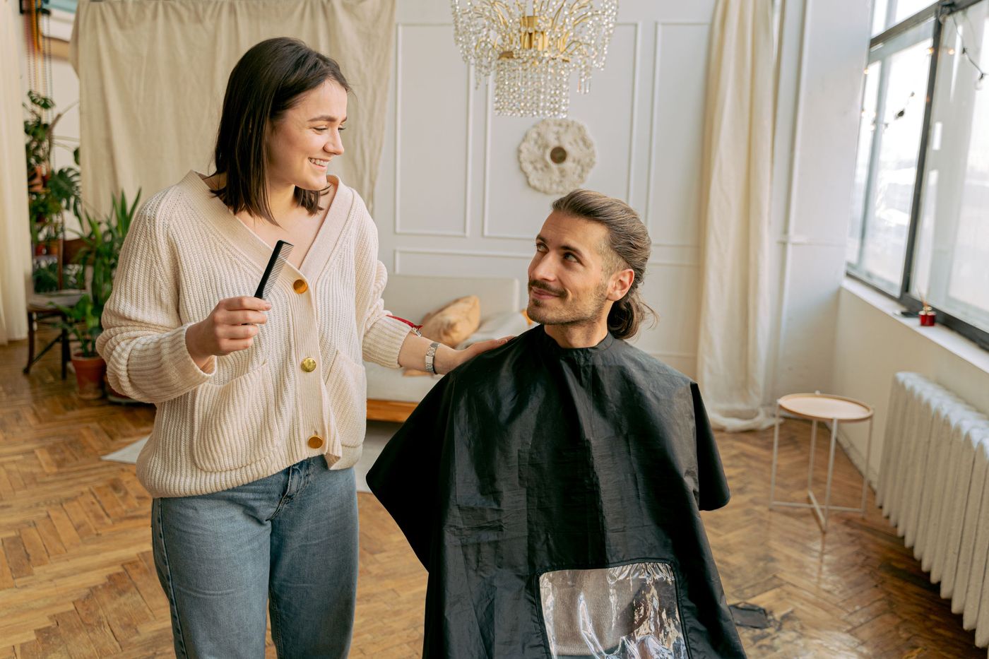 Cabeleireira a arranjar o cabelo de um cliente e a conversar num salão com luz natural