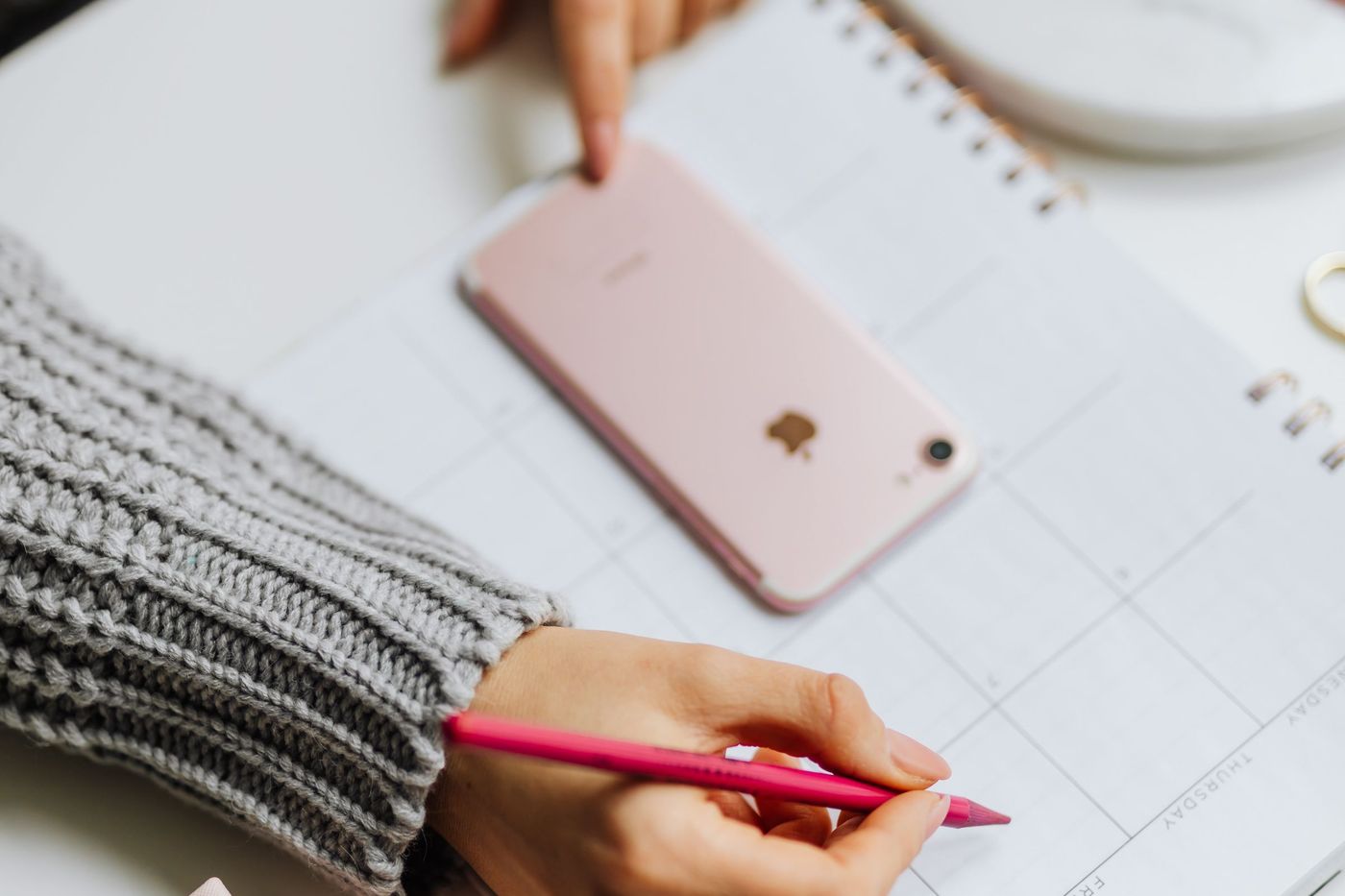 Mão a escrever numa agenda de papel ao lado de um telemóvel