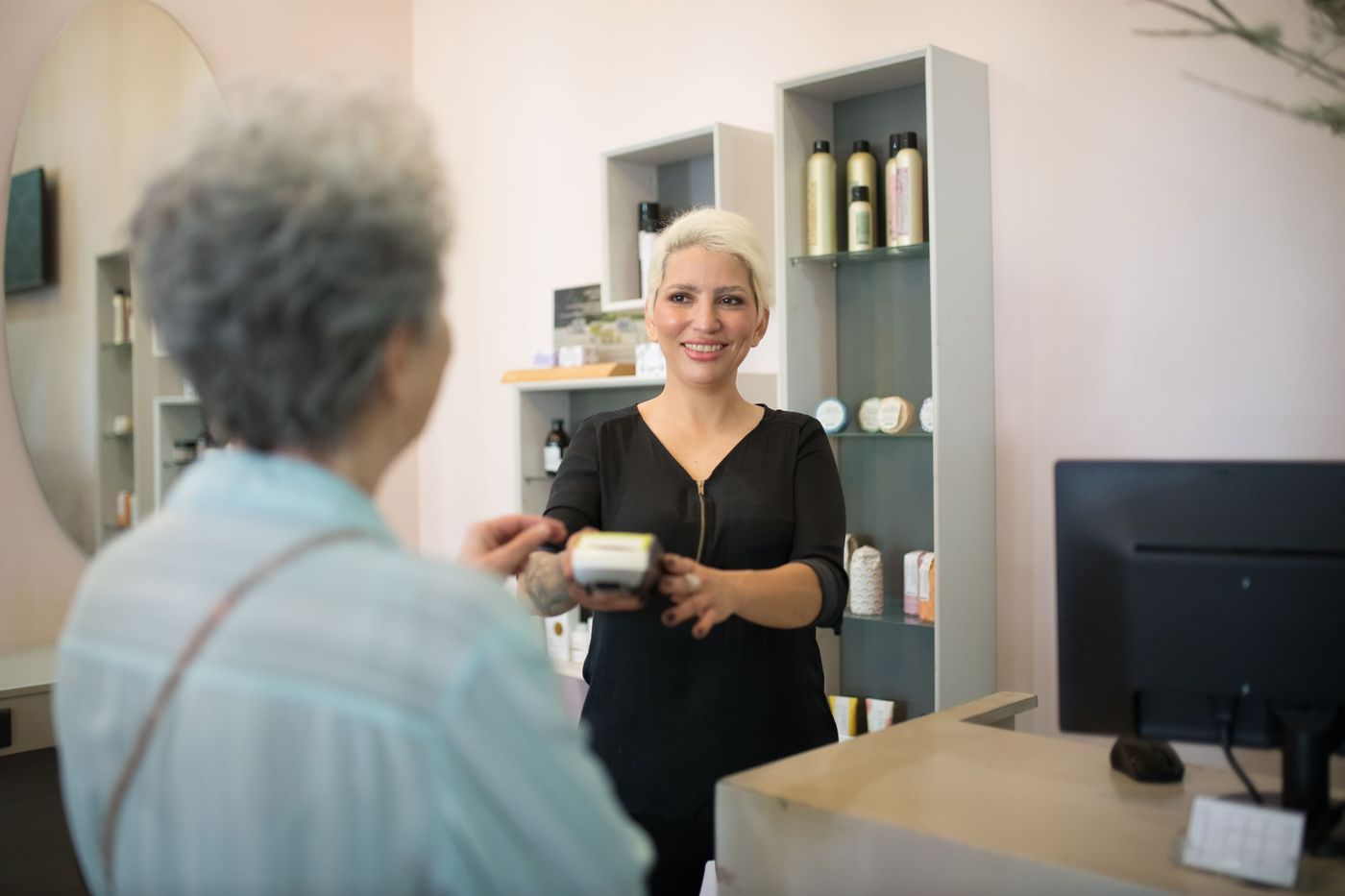 Cabeleireira a receber o pagamento de uma cliente com terminal no balcão do salão