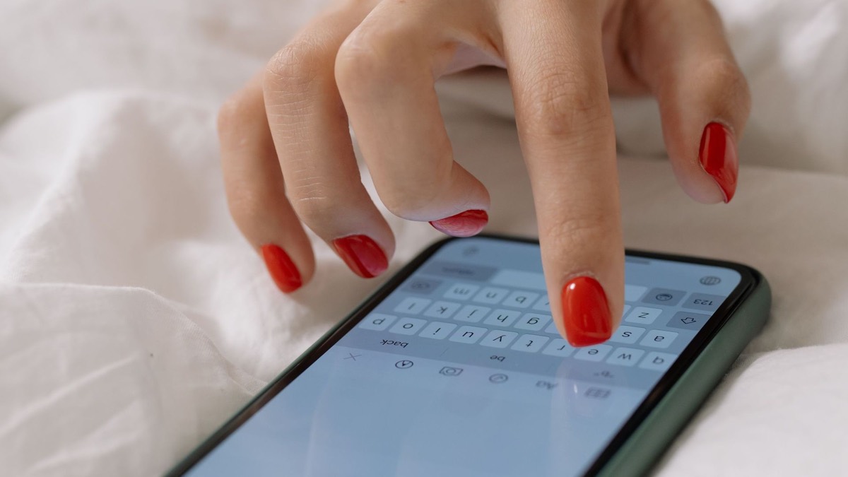 Mão com unhas vermelhas a escrever no telemóvel